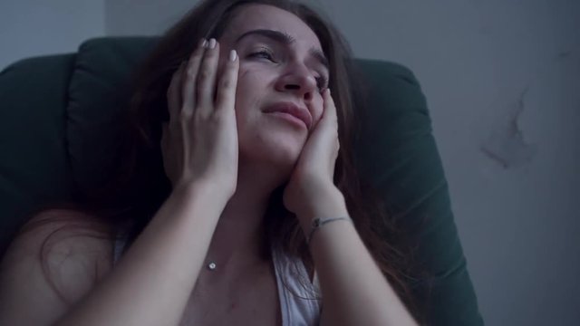 Close-up of young depressed woman in trouble pulling her hair with hands and crying sitting in chair. Lonely woman in despair with suicide thoughts.