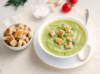 large white bowl with vegetable green cream soup of broccoli, zucchini, green peas on white background, side view
