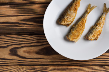 Row of three fried tasty fishes on white ceramic dish on old wooden rustic brown table with copy space for your text