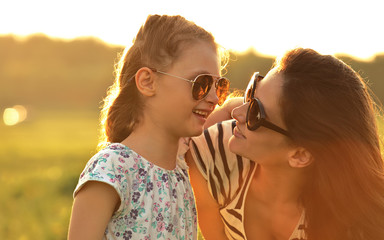 Happy fashion kid girl embracing her mother in trendy sunglasses and looking on nature background. Closeup portrait of happiness.