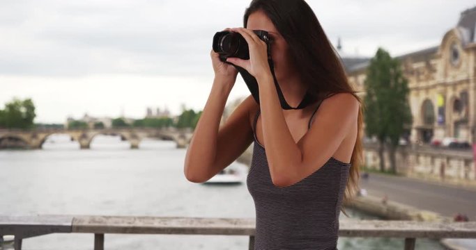 Pretty traveler photographer standing on bridge over the Seine taking picture with camera, Portrait of happy young woman in Paris, France taking photo, 4k