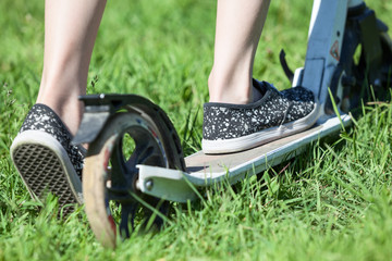 Close-up rear view of child riding kick scooter, green grass on summer meadow