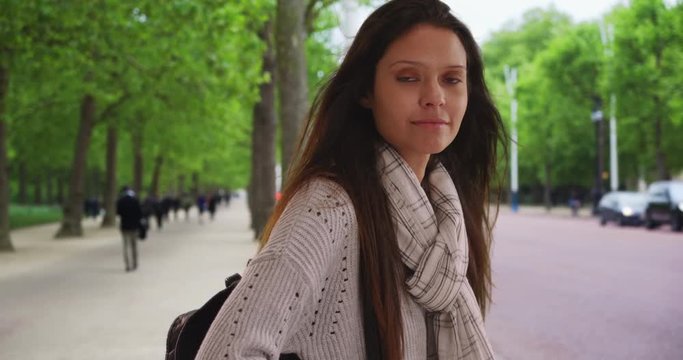 Beautiful female in striped scarf in England making eye contact while on city street, Millennial woman near public park in London smiling at camera, 4k
