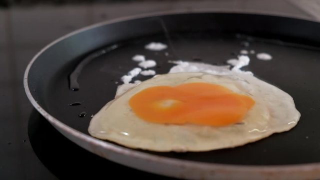 Close-up of dropping one egg in a frying pan for breakfast. Yolk spreading on the pan. Scrambled eggs cooking. 4k video.