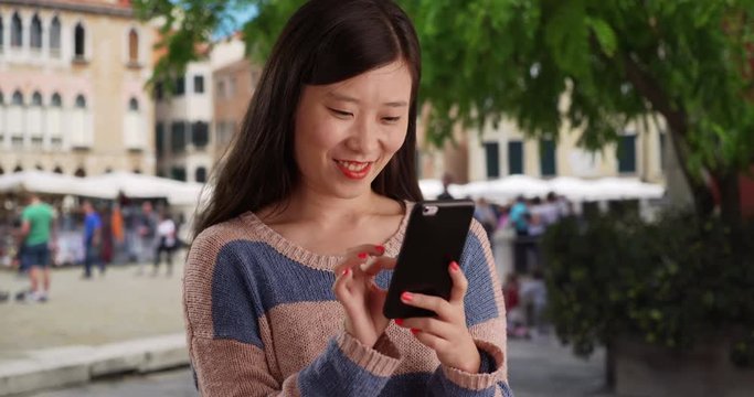 Hip young pretty lady using smartphone and reading text messages in Venice Italy, Close up of lovely Asian female millennial sending texts with cell phone in old European city, 4k