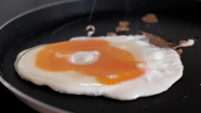 Close-up of salting one egg being fried on a frying pan. Yolk spread on the protein. Scrambled eggs cooking. 4k video.