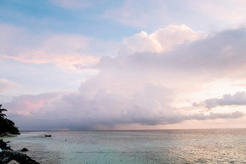 Maldives background. Sunset over the tropical sea and coral beach with colorful clouds in the sky. Boats on the horizon in heavenly atoll of peace and relaxation.