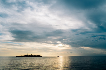 Maldives background. Sunset over the tropical sea and coral beach with colorful clouds in the sky. Boats on the horizon in heavenly atoll of peace and relaxation.