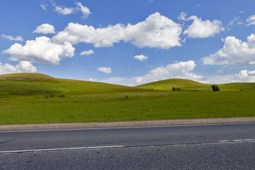 Road in the field, long distance trail in the field. Beautiful green hills. Blue sky with fluffy clouds