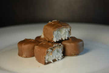 On a white glass plate there are beautiful sweets with coconut filling of white color and milk...
