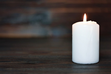 Fototapeta na wymiar White burning candle on wooden background