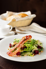 Salad with bacon and vegetables close-up on a wooden table