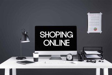 desktop computer with shopping online inscription on screen, business chart, clock and office supplies at workplace