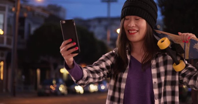 Happy hipster millennial woman taking selfie with smart phone camera in urban setting, Close view of young Asian woman holding skateboard in San Francisco California, 4k