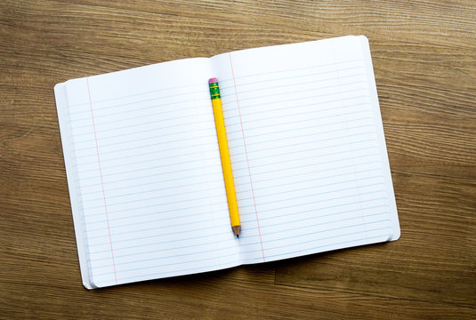 a yellow pencil on top of an open notebook with empty pages for a customized message on a wooden desk