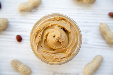 Peanut butter in a bowl and unshelled peanuts on a white wooden background, top view. Close-up.