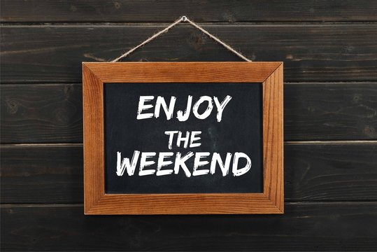 Blackboard With Enjoy The Weekend Inscription Hanging On Wooden Wall