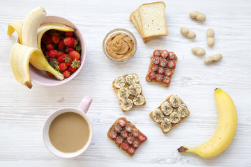 Top view healthy breakfast: latte, vegan toasts with fruits, seeds, peanut butter. White wooden background. From above. Flat lay.