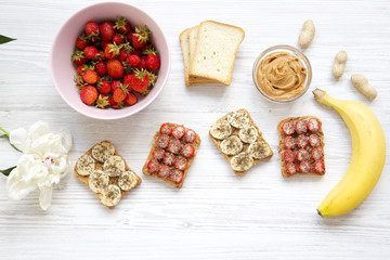 Fototapeta na wymiar Healthy breakfast with ingredients, dieting concept. Vegan toasts with fruits, seeds, peanut butter over white wooden background, top view. From above.