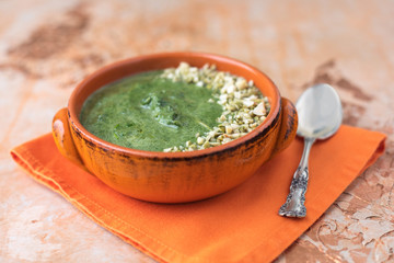 Cream of Spinach Soup in an Orange Bowl Topped with Chopped Pumpkin Seeds and Peanuts