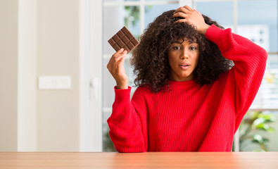 African american woman eating chocolate bar at home stressed with hand on head, shocked with shame and surprise face, angry and frustrated. Fear and upset for mistake.