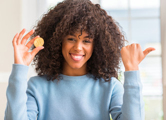 African american woman holding golden bitcoin cryptocurrency at home pointing with hand and finger...