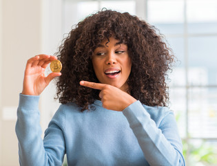 African american woman holding golden bitcoin cryptocurrency at home very happy pointing with hand...