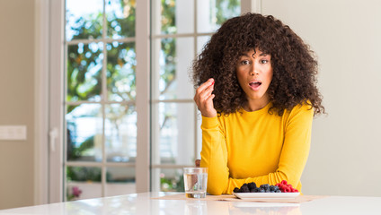 African american woman eating raspberries and blueberries at home scared in shock with a surprise face, afraid and excited with fear expression