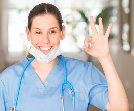 Young nurse woman wearing mask and stethoscope doing ok sign with fingers, excellent symbol