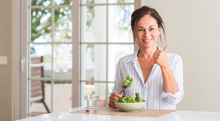 Middle aged woman eating fresh salad in a bowl at home happy with big smile doing ok sign, thumb up...