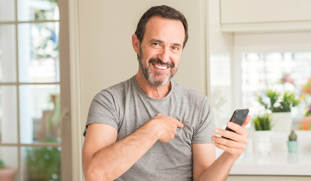 Middle age man using smartphone with surprise face pointing finger to himself