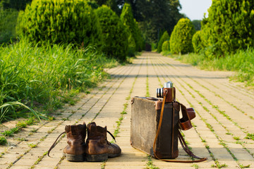 Traveling light! Shabby ankle boots next to a vintage cardboard suitcase, a film camera in its open...