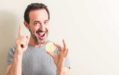 Senior man holding lemon fruit surprised with an idea or question pointing finger with happy face,...