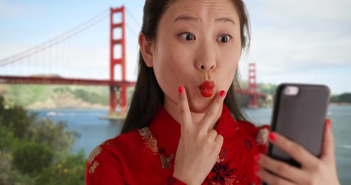 Close up of happy millennial woman smiling for selfie and wearing traditional Chinese fashion by Golden Gate bridge in San Francisco, Young smiling Asian woman using smartphone to take selfie, 4k