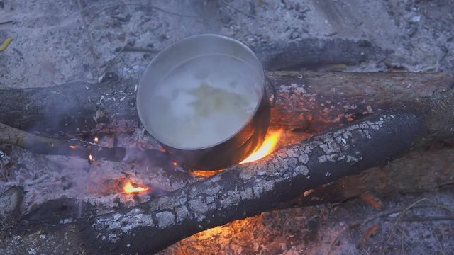 Cooking pasta with cauldron on campfire in evening forest. The cook stirs the food with a spoon. Close-up