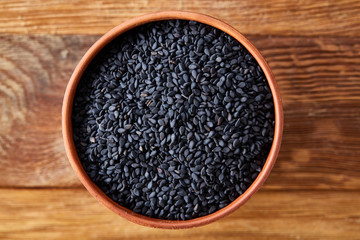 Black sesame seeds in a clay bowl on rustic wooden background, close-up, top view.