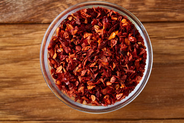 Transparent glass bowl with dried chilly on rustic wooden background, close-up, top view, selective focus.