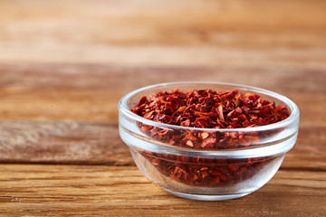 Transparent glass bowl with dried chilly on rustic wooden background, close-up, side view, shallow depth of field.