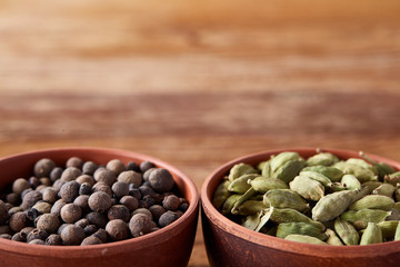 Cardamon and pimento in clay bowls on wooden background, top view, close-up, selective focus.