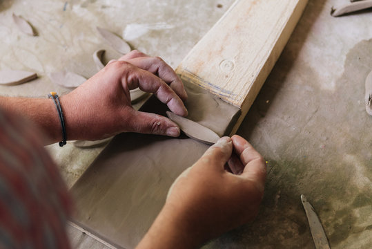 Young man working with clay and creating small ceramic objects in home studio workshop