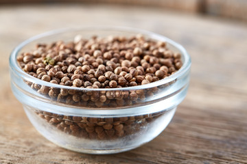 Close-up of glass bowl full of coriander seeds on rustic wooden background, top view, shallow depth of field.