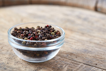 Still life with black pepper seeds in glass jar on wooden barrel, close-up, shallow depth of field.
