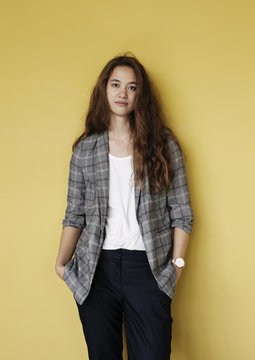 Portrait of a confident young woman against a yellow wall.