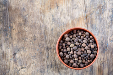 Obraz na płótnie Canvas Clay bowl with dried allspice berries on vintage wooden background, top view, close-up, macro, selective focus.