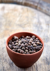 Clay bowl with dried allspice berries on wooden barrel, top view, close-up, macro, selective focus, vertical.