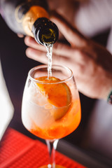 The barman pours champagne into the cocktail of Aperol Spritz close up