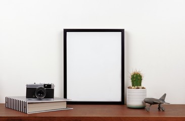 Mock up black frame with travel theme decor on a shelf or desk. Wood shelf and white wall. Portrait...