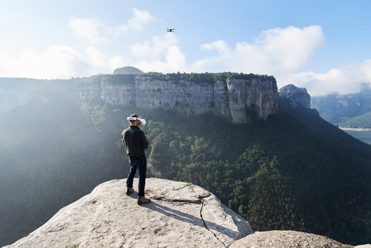 Back view of man controlling flying quadcopter in mountains.