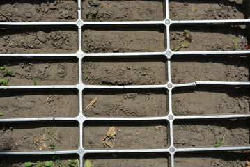 Against the backdrop of the fluffy earth lies a metal grille of metal parallelepipeds in grid format with a reflection of the sun