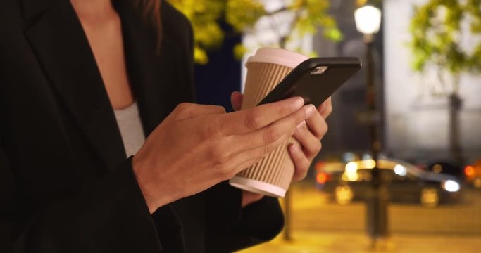 Close up of female hands using mobile phone to text message at night in Paris, Woman on business trip texting while near arc de triomphe and holding coffee cup, 4k